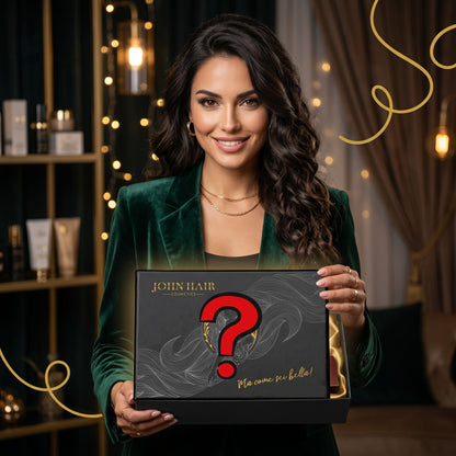 John Hair Mystery Box gift set held by a smiling woman in a green velvet blazer in a luxury salon setting.