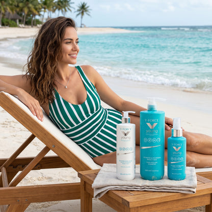 John Hair Y-Force anti-age hair care set with shampoo, conditioner, and spray on a beach lounge chair by the ocean.